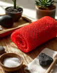 Red african exfoliating net, stones, and a wooden tool on a bamboo mat with plants in the background for peaceful gentle exfoliation towards softer and smoother skin