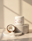 Coconut Cloud Whipped Sugar Scrub on stacked marble with a coconut half spilling white sugar in warm sunlight