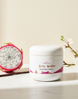 Dragonfruit Vanilla Whipped Body Butter jar beside a halved dragonfruit, vanilla bean and almond blossom branch