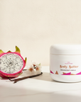 Dragonfruit Vanilla Whipped Body Butter jar with dragonfruit, vanilla bean and blossoms in soft light