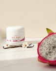 Dragonfruit Vanilla Whipped Body Butter on marble with vanilla pods and blossoms, dragonfruit in the foreground