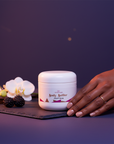 Galaxy Glow Whipped Body Butter on slate at night with blackberries, white orchid and vanilla, a hand reaching for the jar