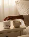 Hand reaching for Coconut Cloud Whipped Body Butter on a bedside table next to a cup of warm milk