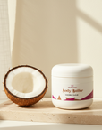 Coconut Cloud Whipped Body Butter on a travertine tray beside a halved coconut in soft window light