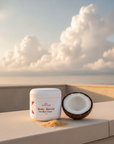 Coconut Cloud Whipped Sugar Scrub on a rooftop ledge with a halved coconut and sugar under soft white clouds