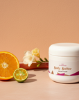 Galaxy Glow Whipped Body Butter beside a halved orange, limequat, rhubarb stalk and white freesia